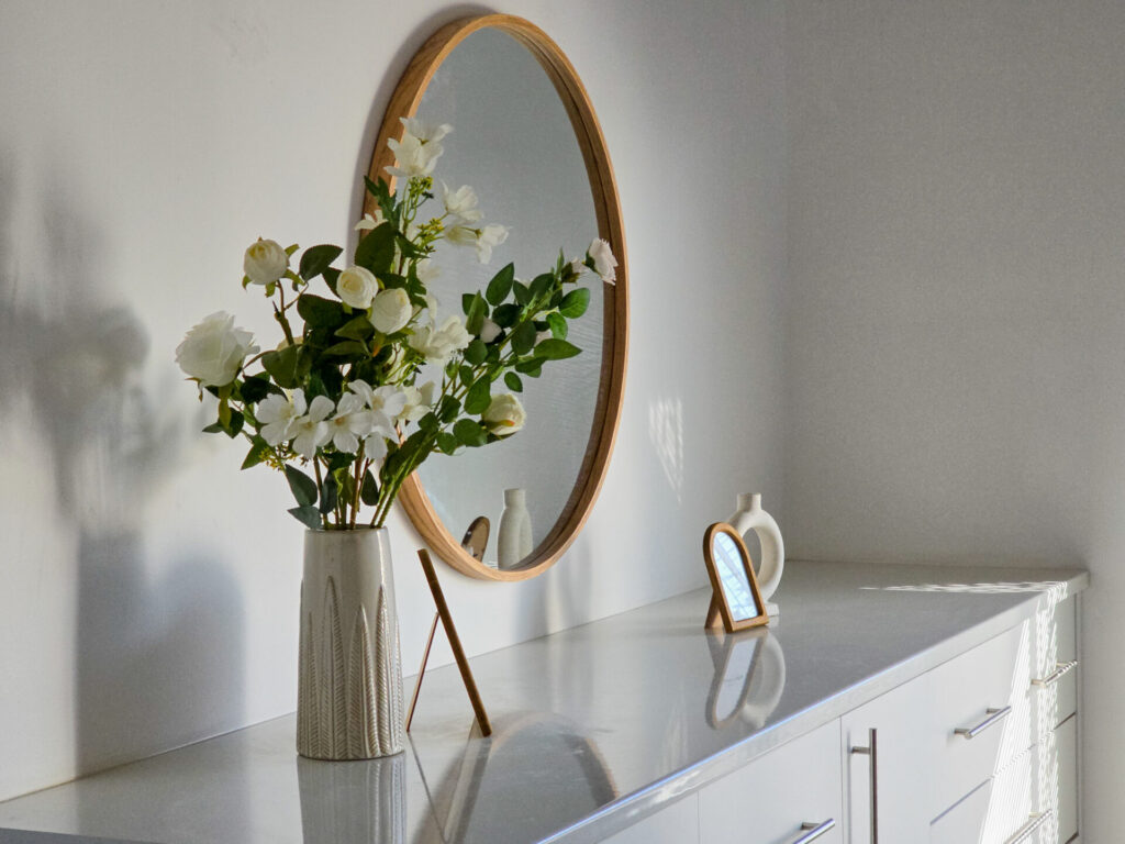 White sideboard styled with flowers beneath a round mirror