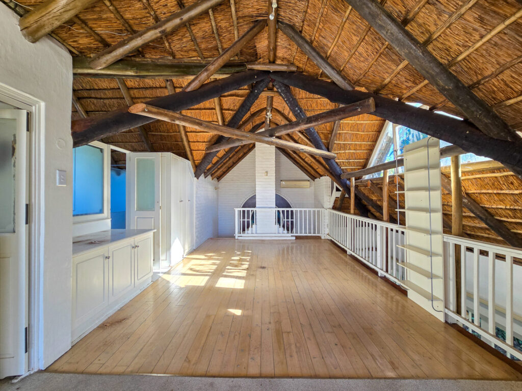 Sunlit upper landing beneath exposed timber beams and a thatched roof