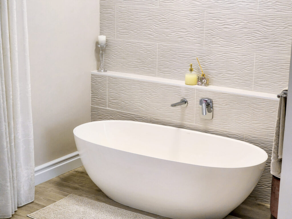 Freestanding oval bathtub against a pale tiled wall