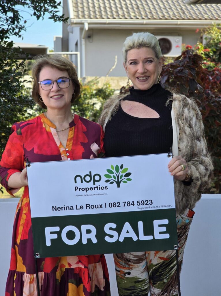 Two women holding an NDP Properties for-sale board outside a home