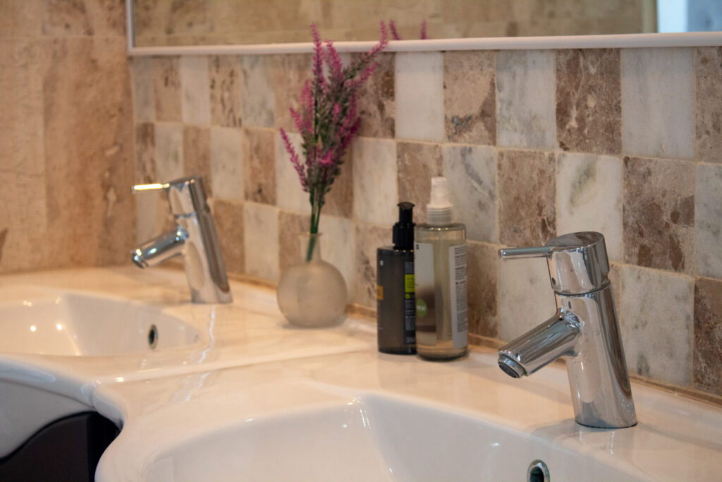 Twin bathroom basins with chrome taps and natural stone wall tiles