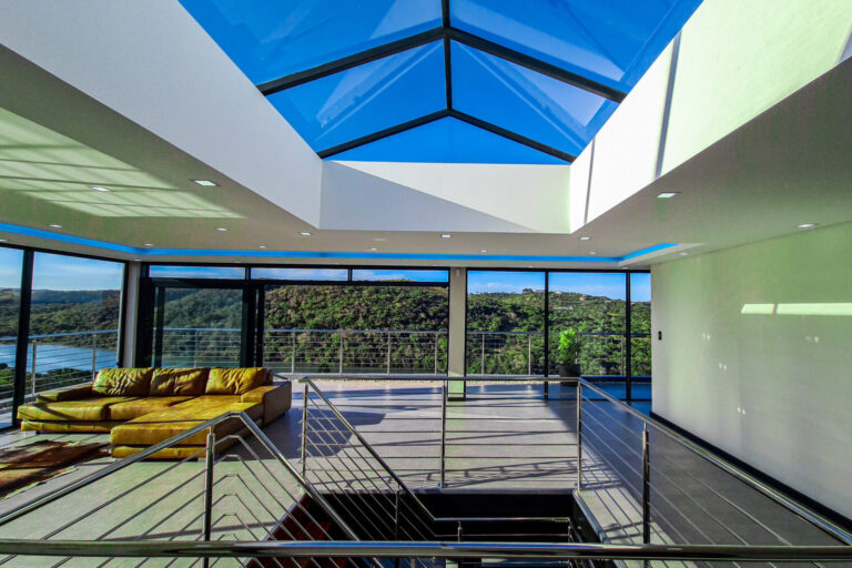 Glass-roofed living area with a balcony overlooking a river and wooded hills